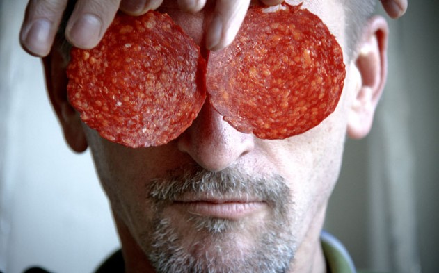 Man met sikje houdt 2 plakken chorizo voor zijn ogen.